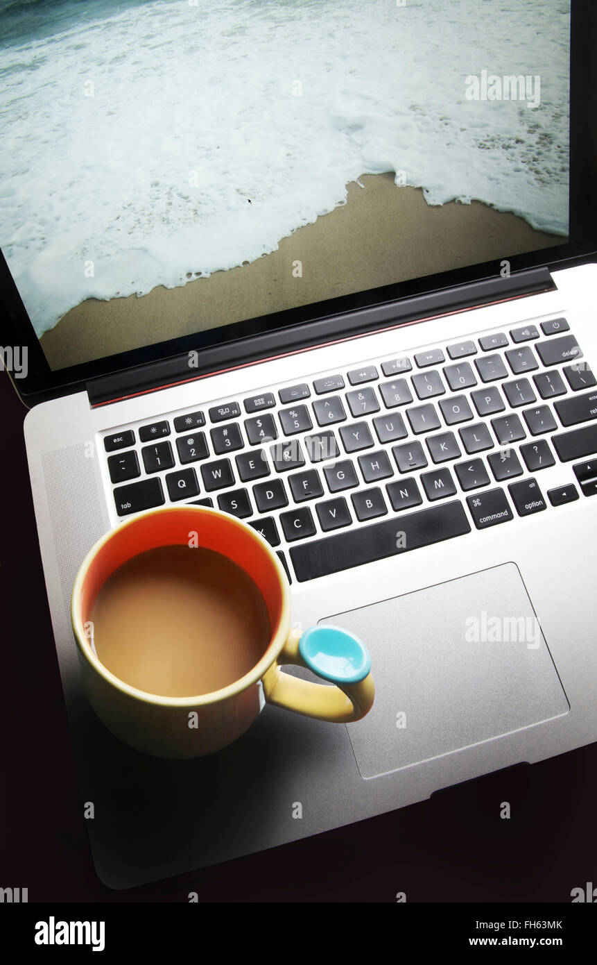 Kaffeebecher auf Laptop-Computer mit Strand auf Bildschirm Stockfoto
