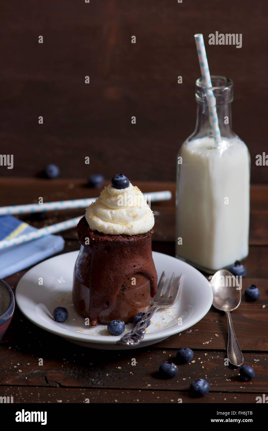 Schokoladen-Kuchen im Glas mit Schlagsahne, Rohrzucker und Heidelbeeren und eine Flasche Milch Stockfoto