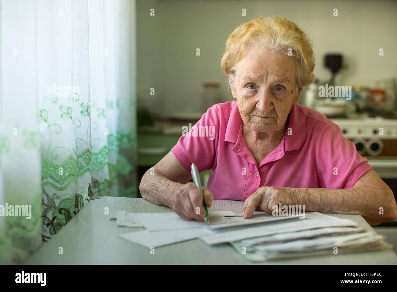 Die alte Frau füllt Stromrechnungen in der Küche sitzen. Stockfoto
