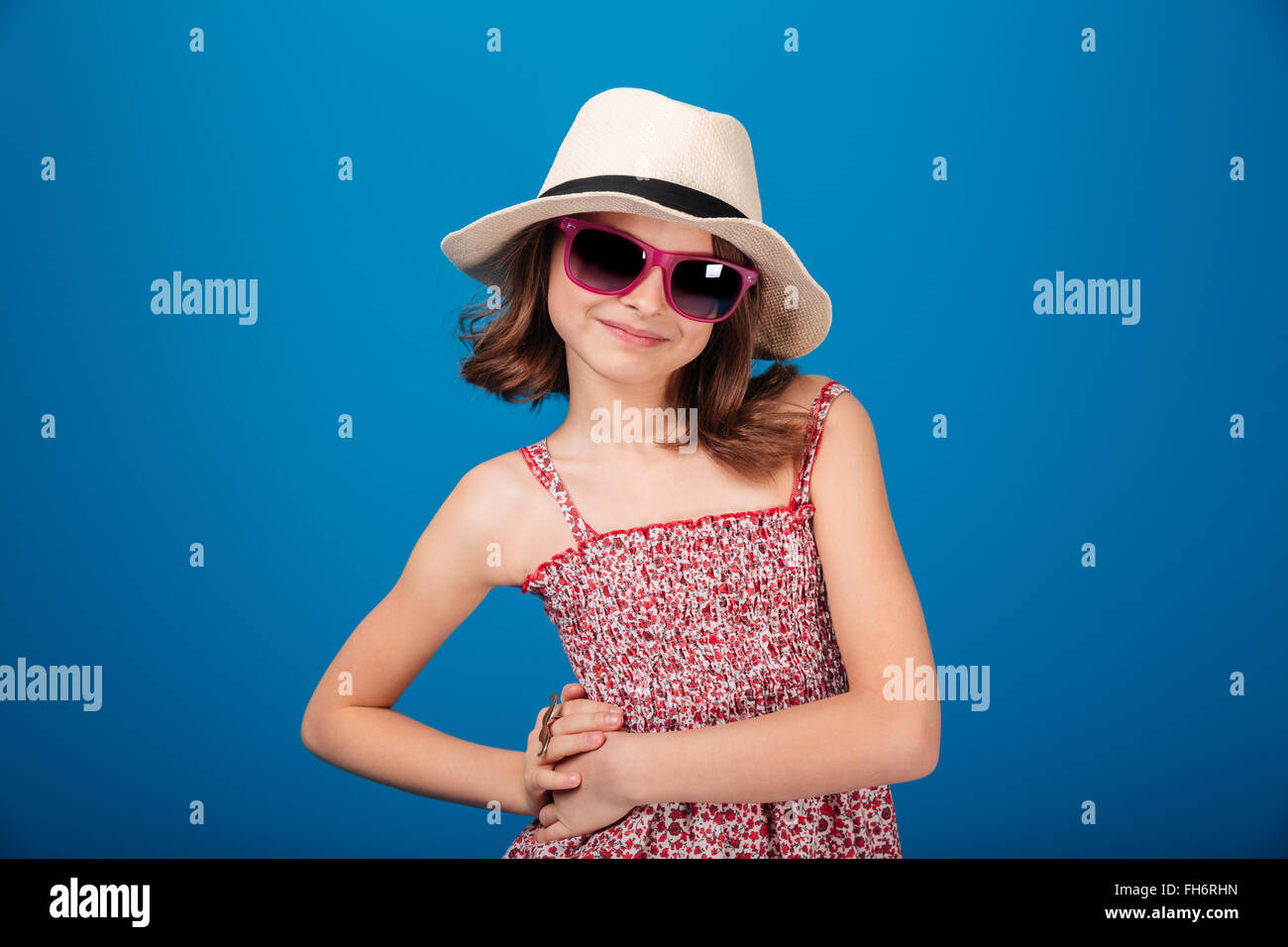 Porträt von glücklich niedliche kleine Mädchen in Hut und Sonnenbrille posiert auf blauem Hintergrund Stockfoto