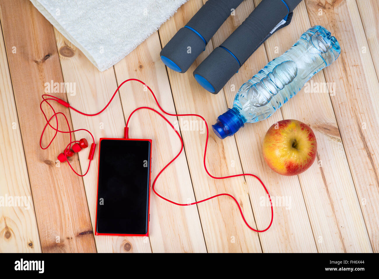 Sportgeräte. Hanteln, Flasche Wasser, weißes Handtuch, Apple, Handy und Kopfhörer auf Brettern. Stockfoto