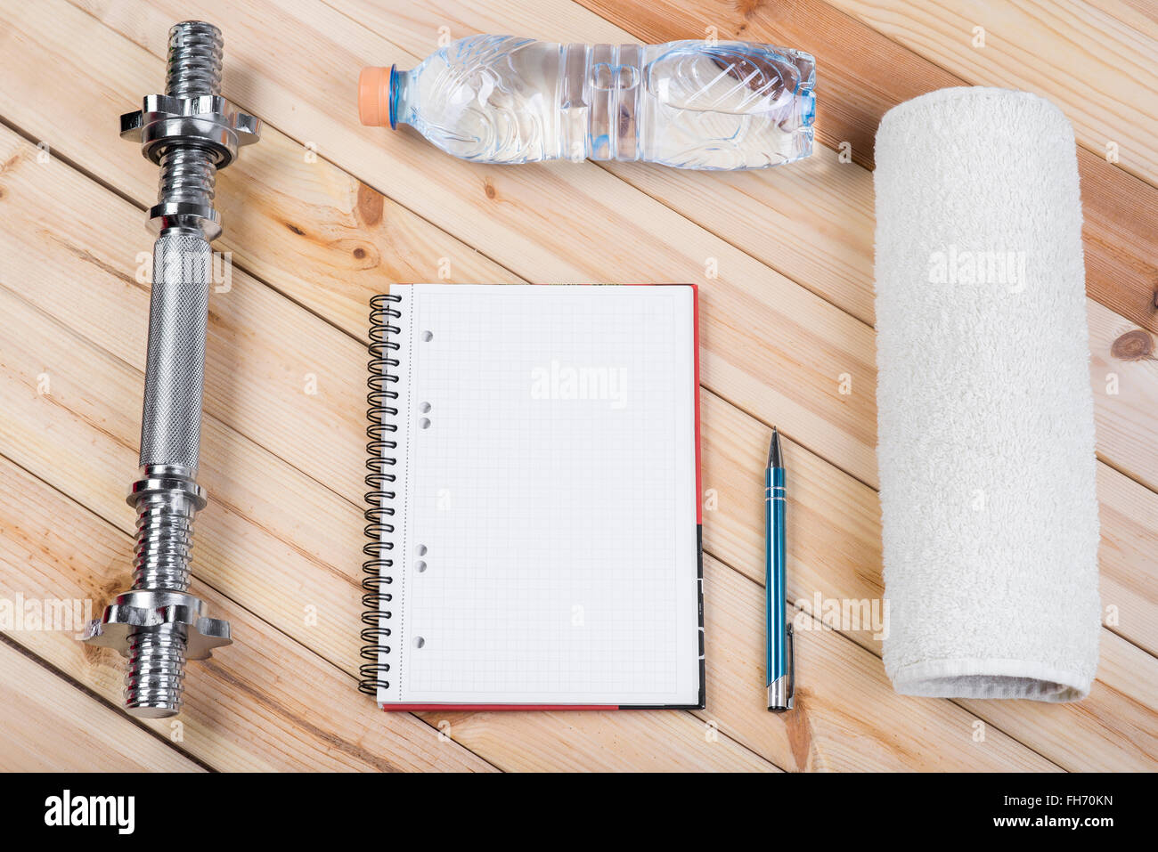 Einfach Fitnesskonzept mit Ausrüstung. Langhantel, Flasche Wasser, Handtuch und Notebook zu Trainingsplan auf Holztisch. Stockfoto