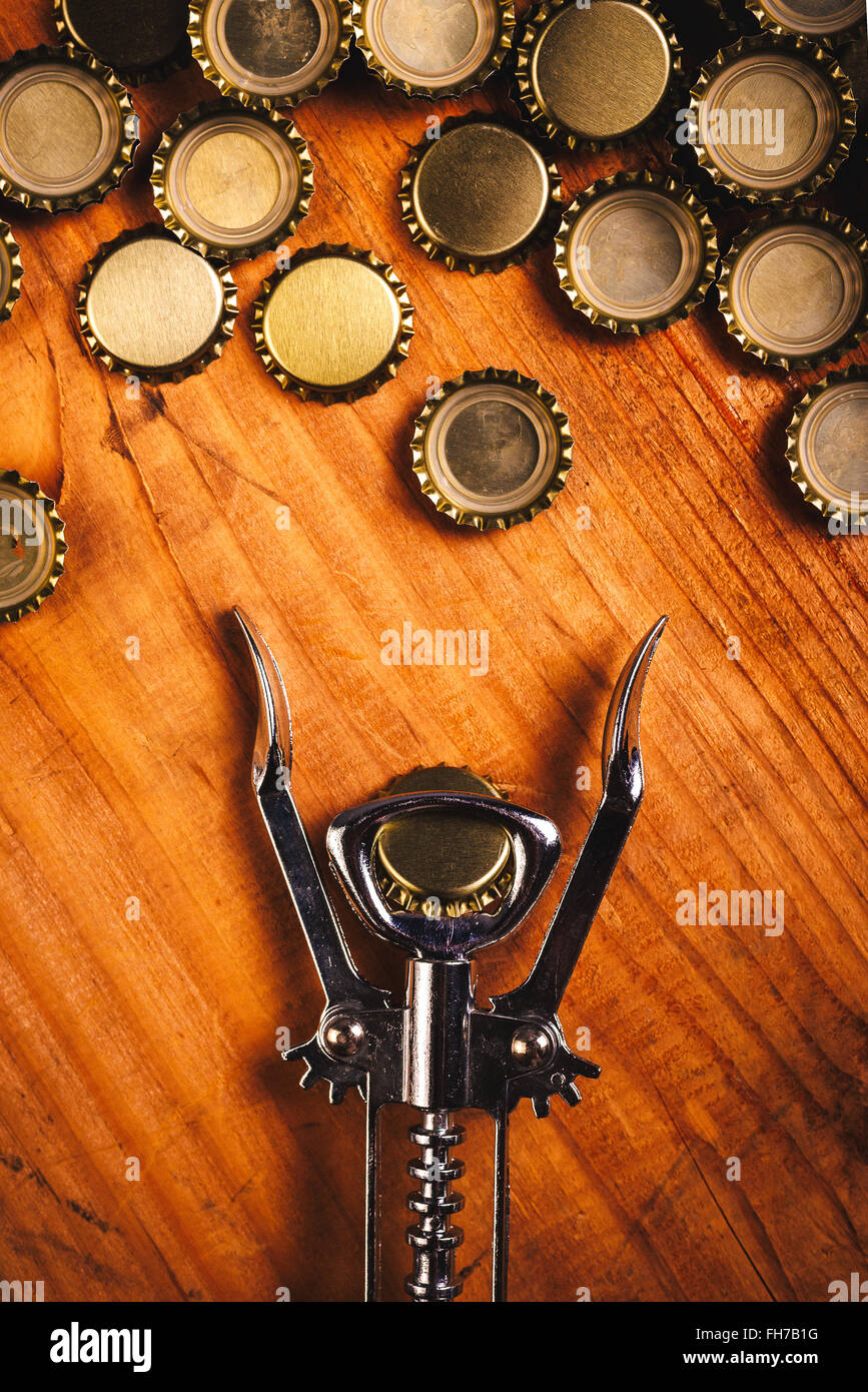Klassische Flaschenöffner und Haufen von Bier Kronkorken auf rustikalen Eiche Holz Schreibtisch, Ansicht von oben. Stockfoto
