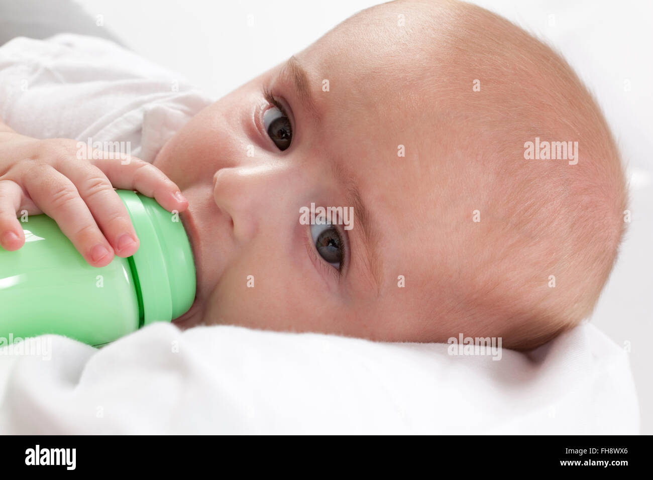 Baby Junge Blick in die Kamera beim Trinken aus einer Babyflasche auf weißem Hintergrund Stockfoto