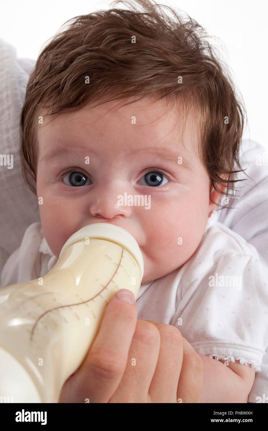 Babymädchen auf der Suche in die Kamera beim Trinken aus einer Babyflasche auf weißem Hintergrund Stockfoto