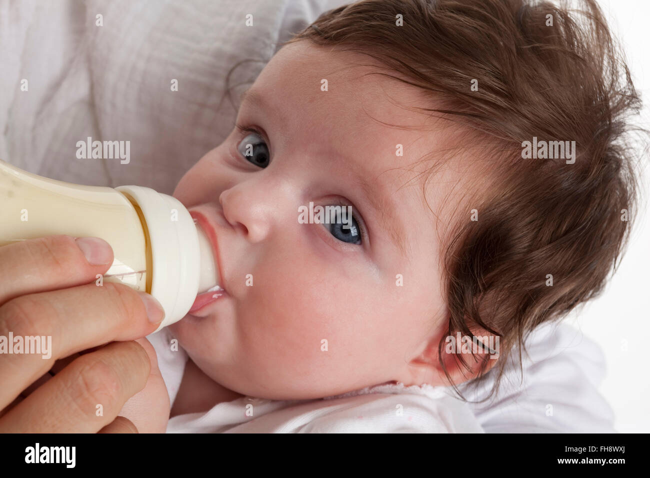 Babymädchen auf der Suche in die Kamera beim Trinken aus einer Babyflasche auf weißem Hintergrund Stockfoto