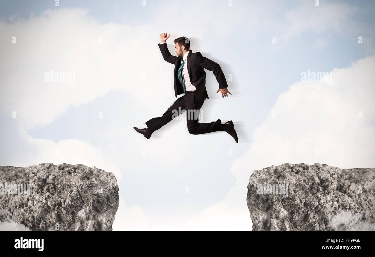 Funny Business Mann springt über Felsen mit Lücke Stockfoto