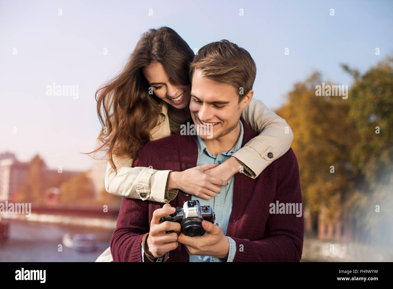 Deutschland, Berlin, glückliches junges Paar Blick in die Kamera am Ufer des Flusses Spree Stockfoto
