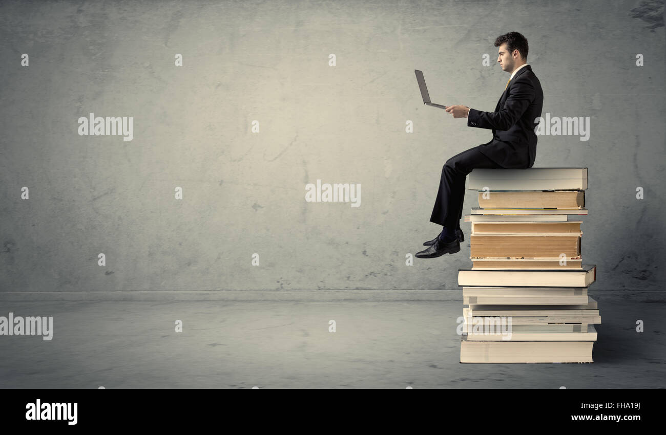 Mann mit Laptop sitzen auf Bücher Stockfoto