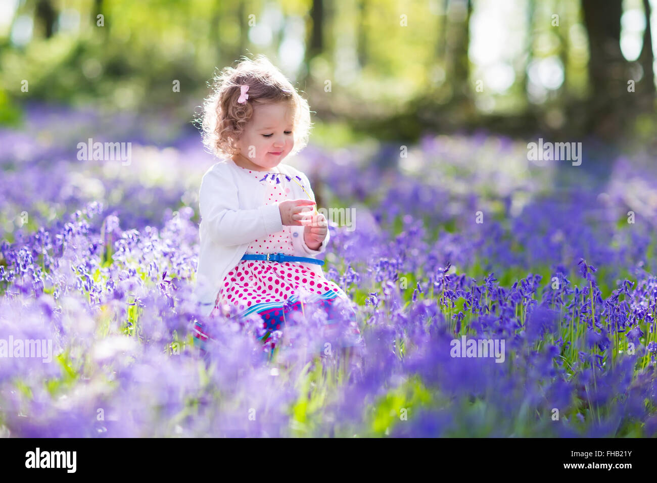 Kleine Mädchen spielen im blühenden Garten. Baby auf Osterei jagen in blue Bell Blumenwiese. Kleinkind Kind Kommissionierung Glockenblumen Stockfoto