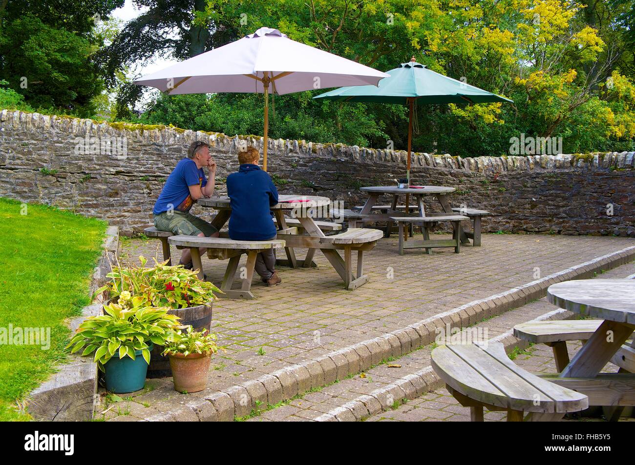 Northumberland. Mittleren gealterten paar sitzt am Picknicktisch unter Sonnenschirm. Der weiße Mönch Teestube, Blanchland. Stockfoto