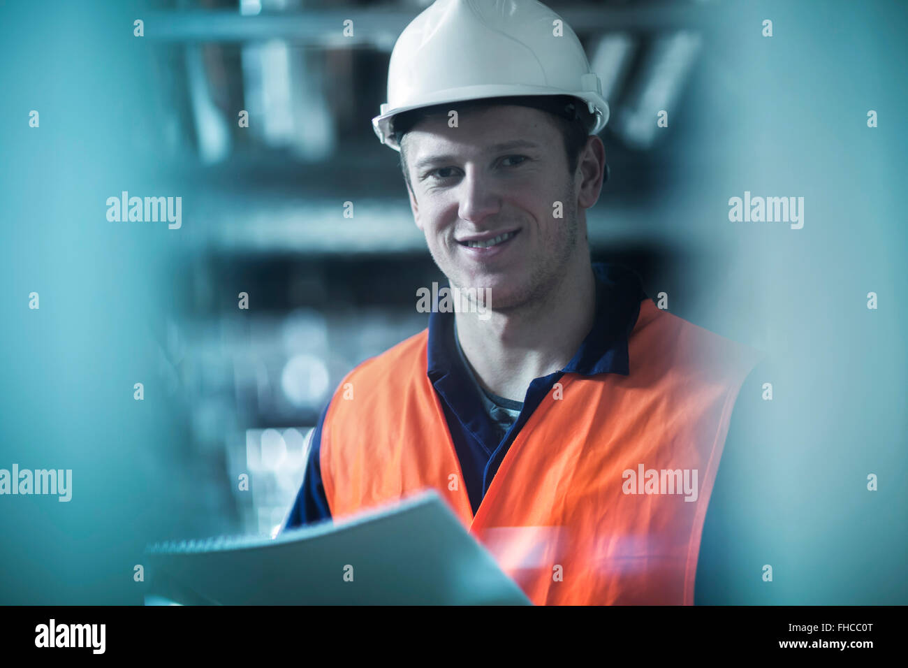 Porträt von lächelnden jungen Mann mit Sicherheitskleidung im Technikraum Stockfoto