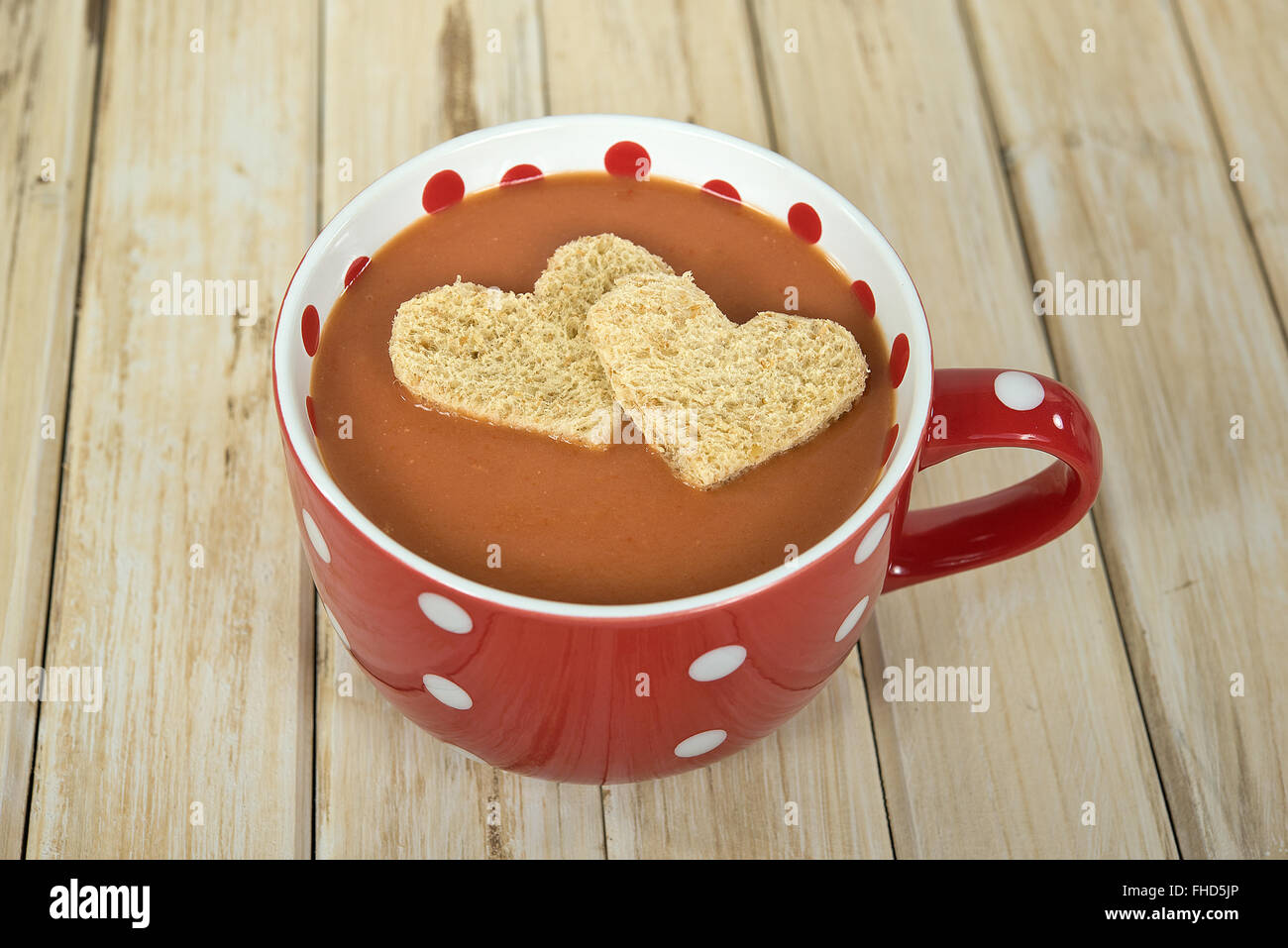 Paar Herz geformt Brot in Tomatensuppe in roten und weißen Tupfen Suppe Becher schweben. Stockfoto