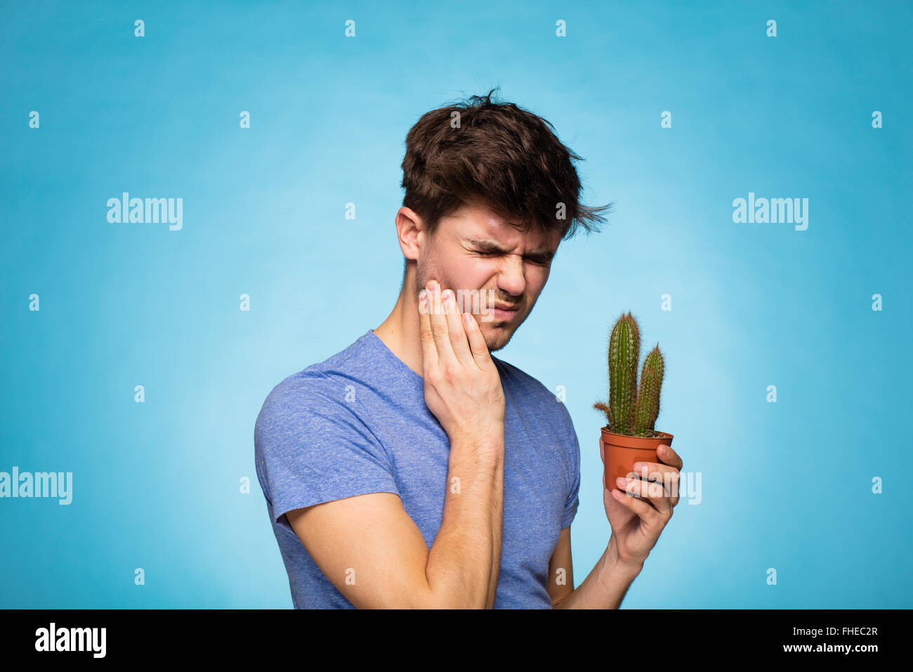 Konzept mit einem jungen Mann im T-shirt, hält in der hand einen Kaktus vor Schmerzen Stockfoto