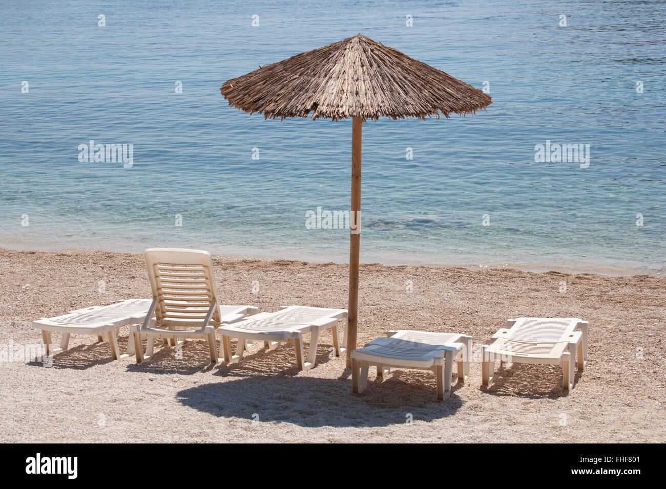 Holz Sonnenschirm mit mehreren liegen an einem einsamen sonnigen Strand mit klarem Wasser. Stockfoto