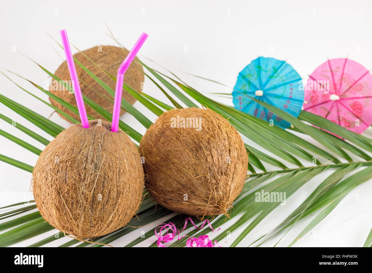 Frische Kokosnuss Cocktails mit Sonnenschirmen auf Kokosnussblättern platziert Stockfoto