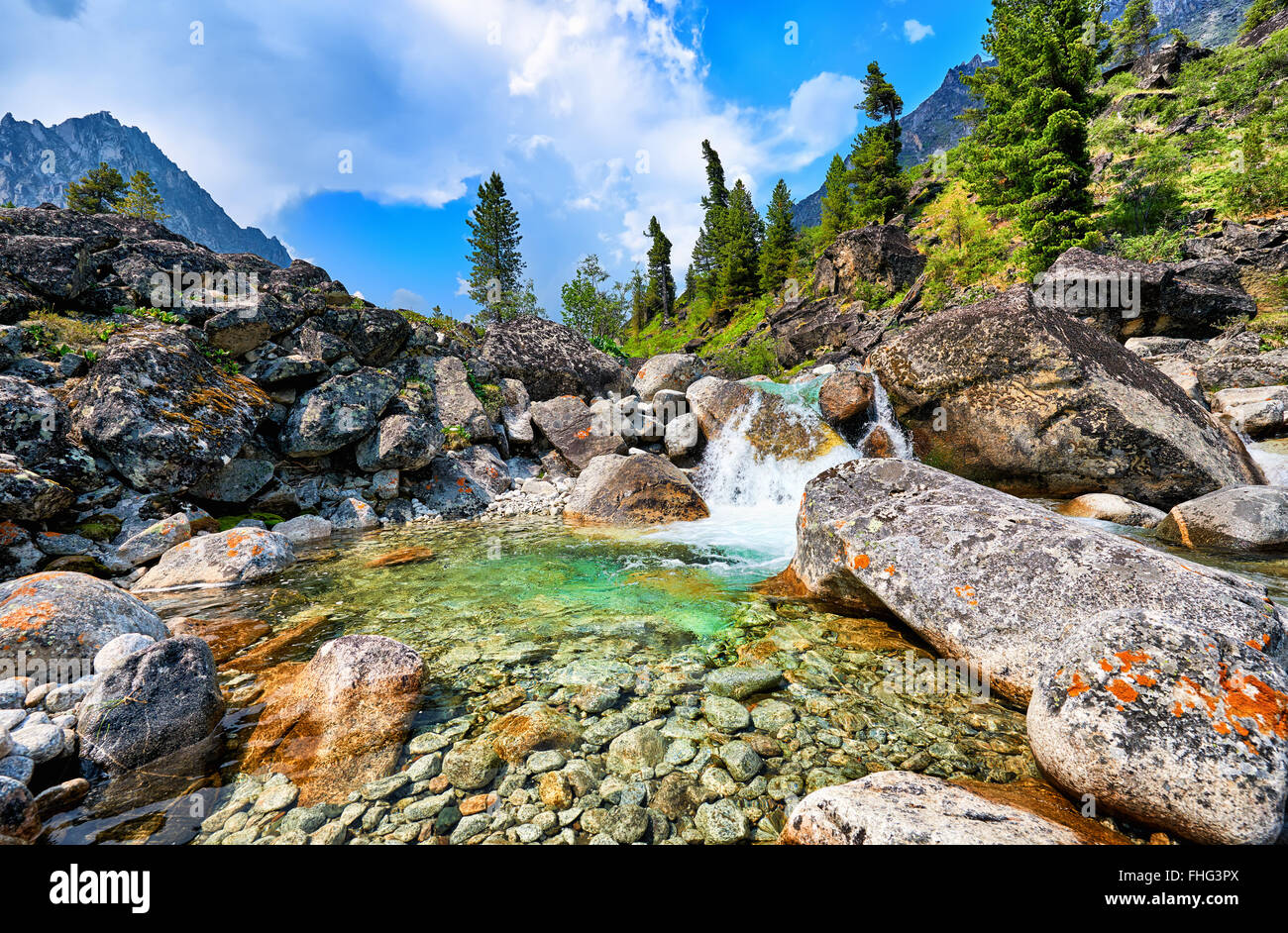 Klares Wasser aus einem Gebirgsbach und ein kleiner Wasserfall in einem natürlichen Becken zwischen großen Felsbrocken. Östlichen Sayan Stockfoto