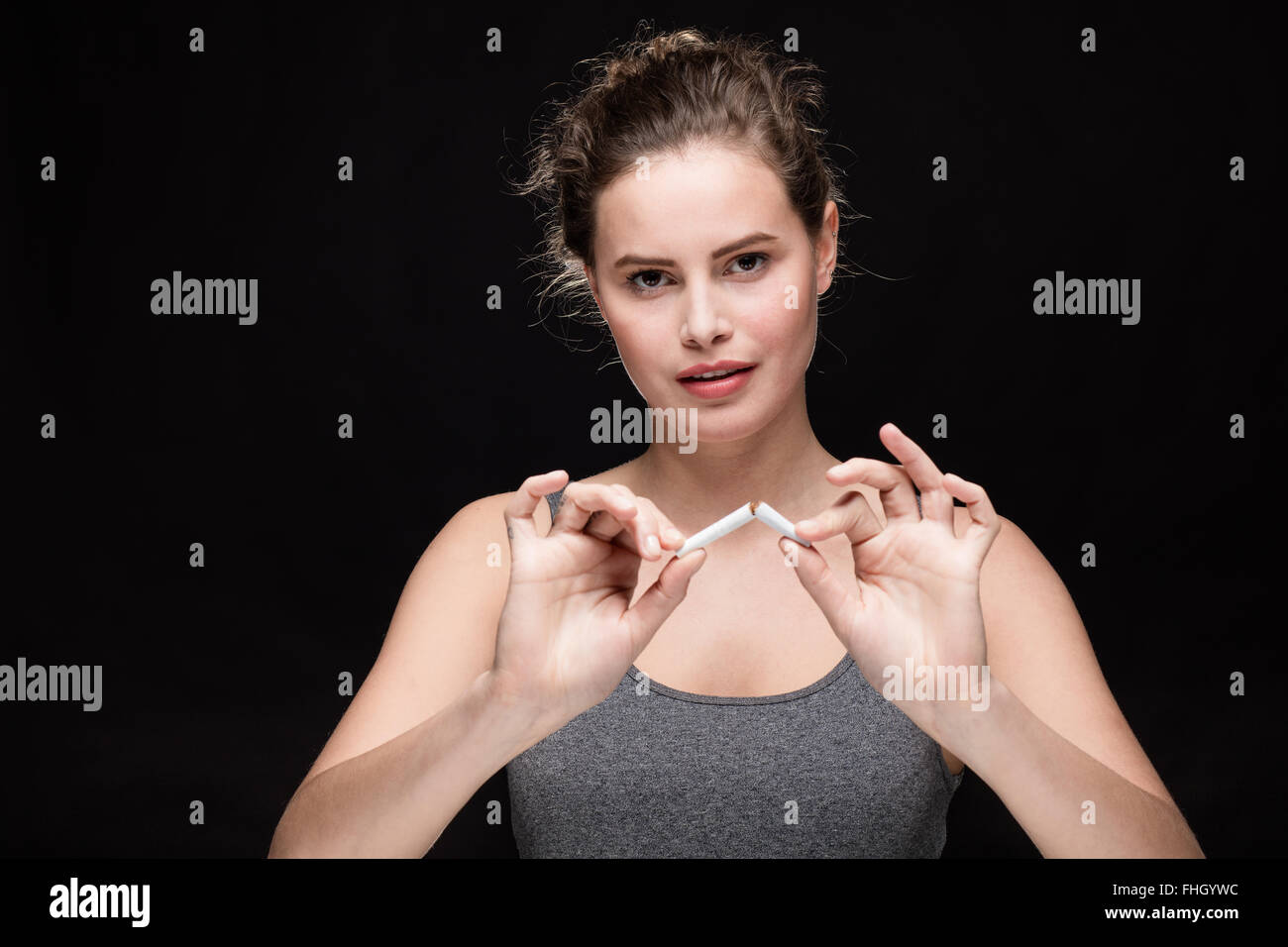 junge Frau bricht eine Zigarette, Rauchen Konzept auf schwarzem Hintergrund Stockfoto