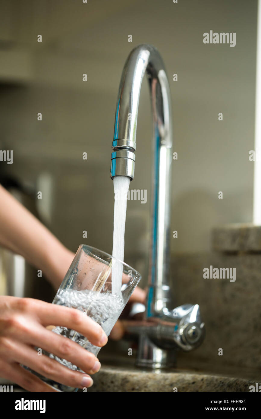 Hübsche blonde Frau füllt ein Glas Wasser Stockfoto