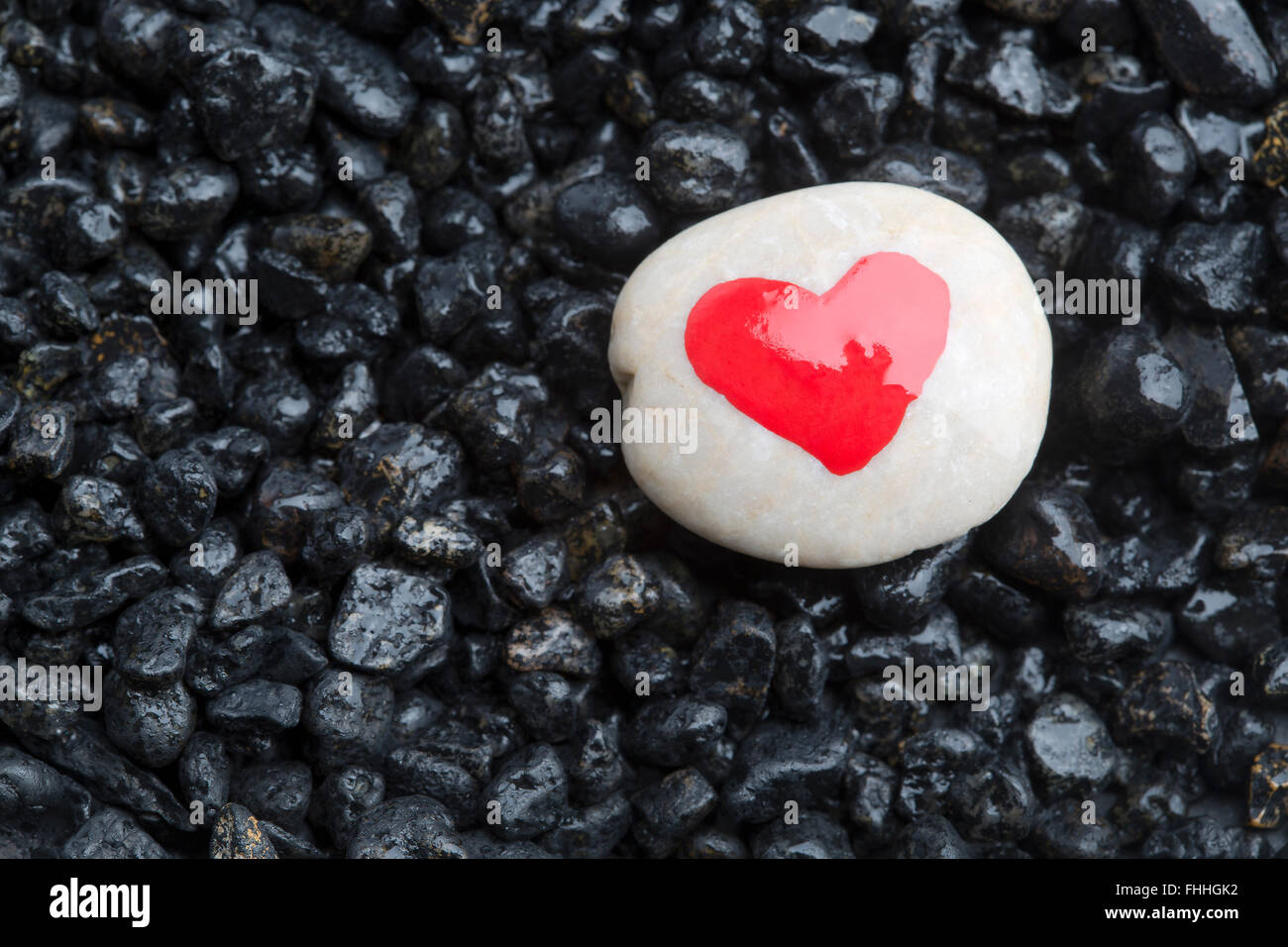 Rotes Herz auf einem weißen Stein mit dunklen Steinen für Hintergrund Stockfoto