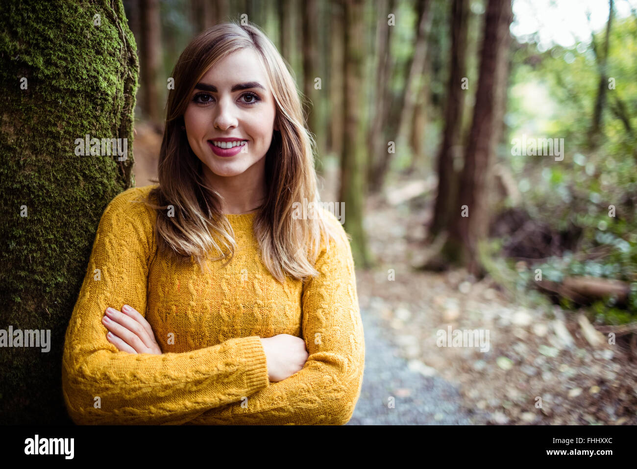 Hübsche blonde Frau, die an einen Baum gelehnt Stockfoto