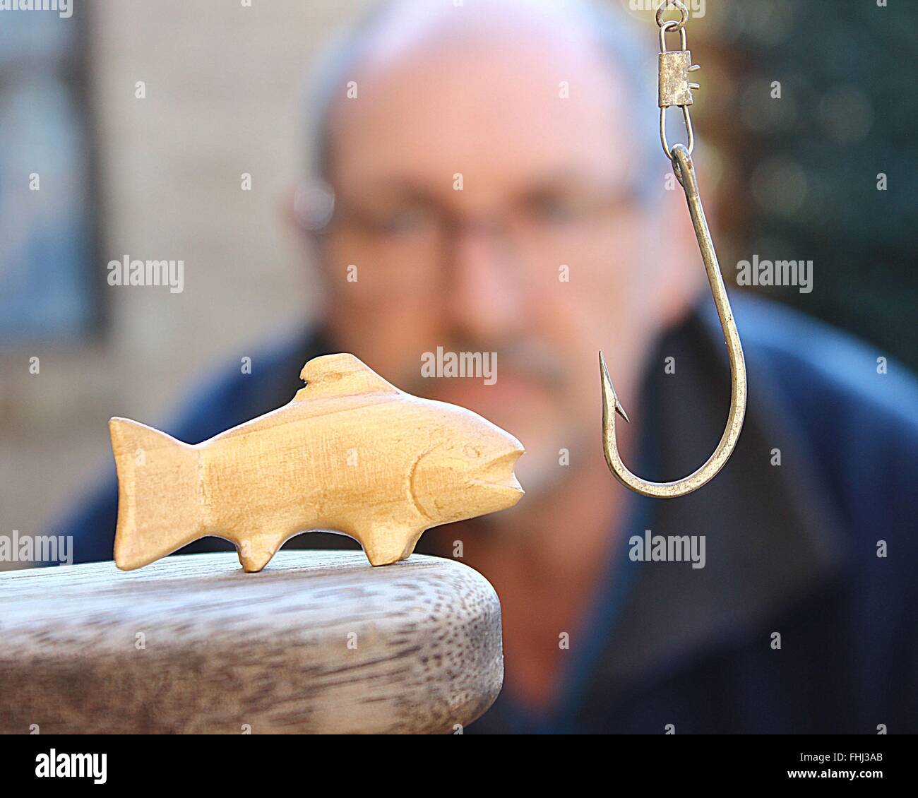Mann, die geschnitzten Fisch und überdimensionierten Angelhaken zu betrachten Stockfoto