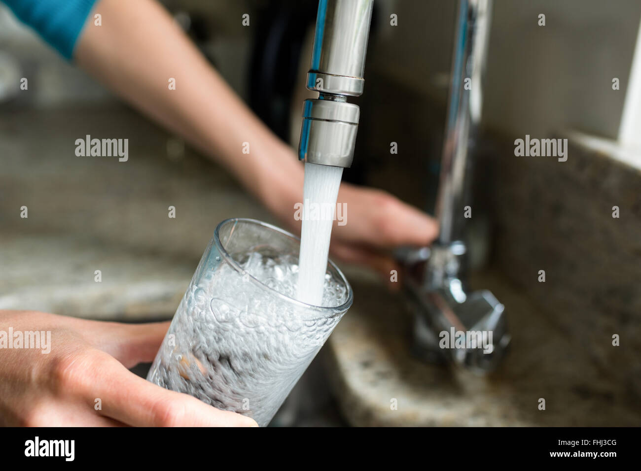 Hübsche blonde Frau füllt ein Glas Wasser Stockfoto