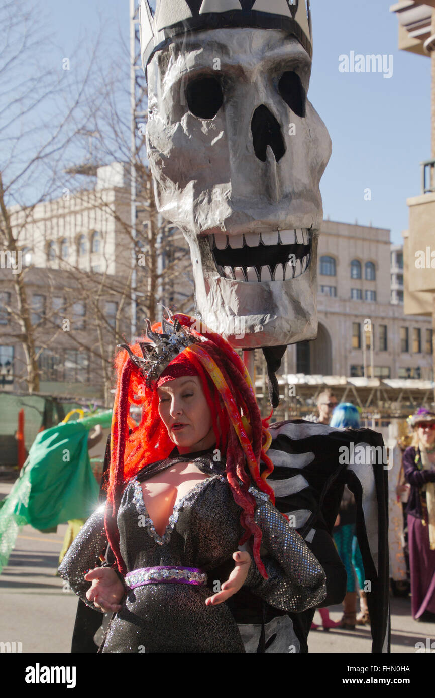 Eine riesige Schädel Marionette grins toothily hinter einer Frau, gekleidet in einem bunten Kostüm in Asheville Karneval parade Stockfoto