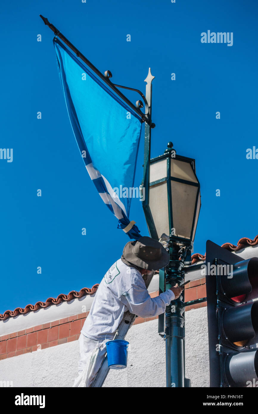 Männlichen spanischen Maler steht auf einer Leiter über seine Tropfen Tuch wie er einen Ampel-Pol malt. Stockfoto