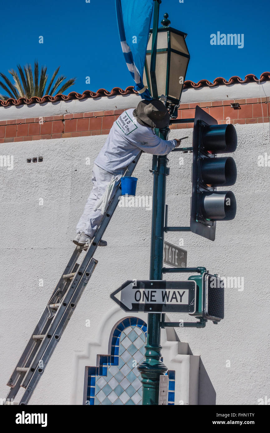 Männlichen spanischen Maler steht auf einer Leiter über seine Tropfen Tuch wie er einen Ampel-Pol malt. Stockfoto