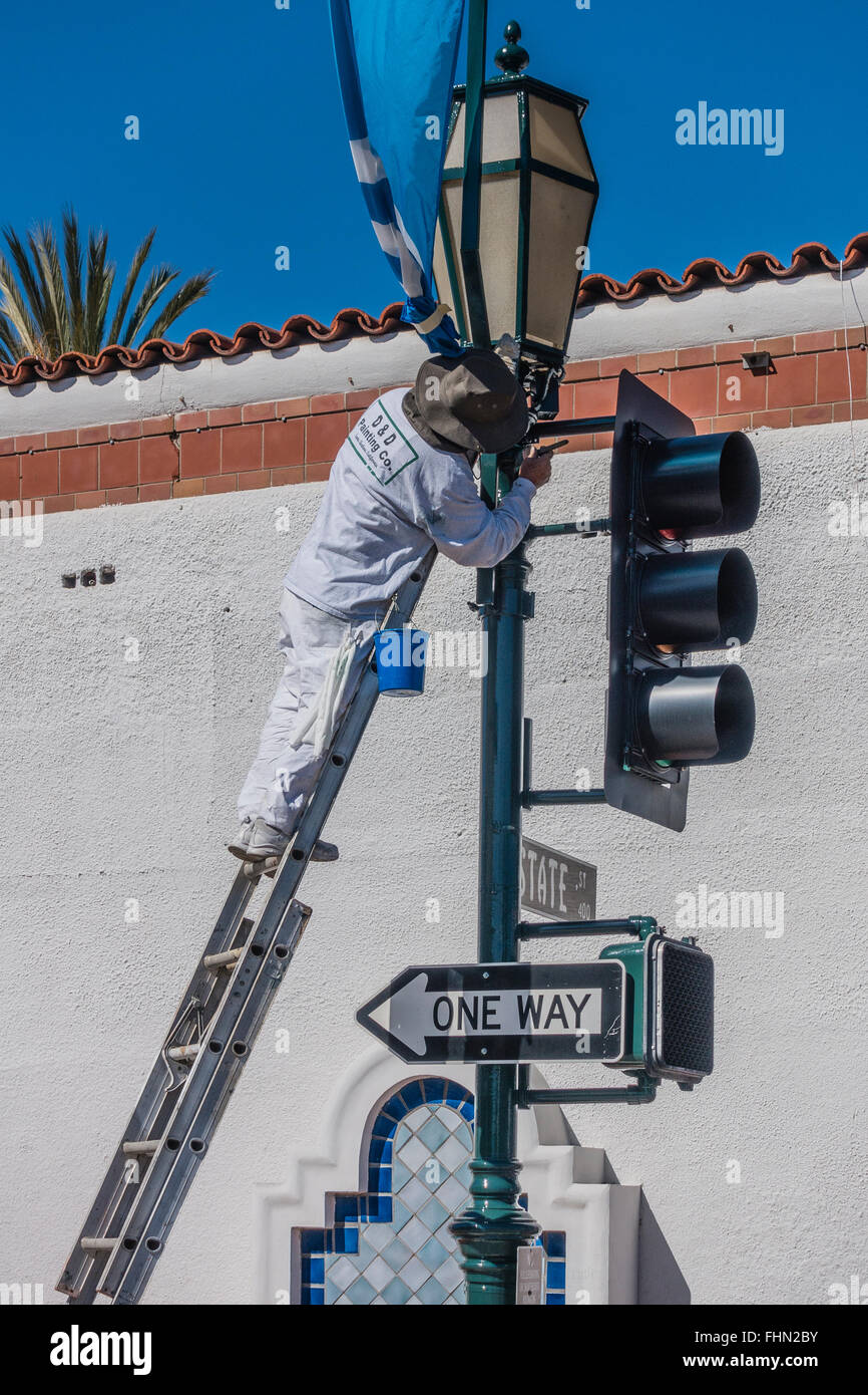 Männlichen spanischen Maler steht auf einer Leiter über seine Tropfen Tuch wie er einen Ampel-Pol malt. Stockfoto