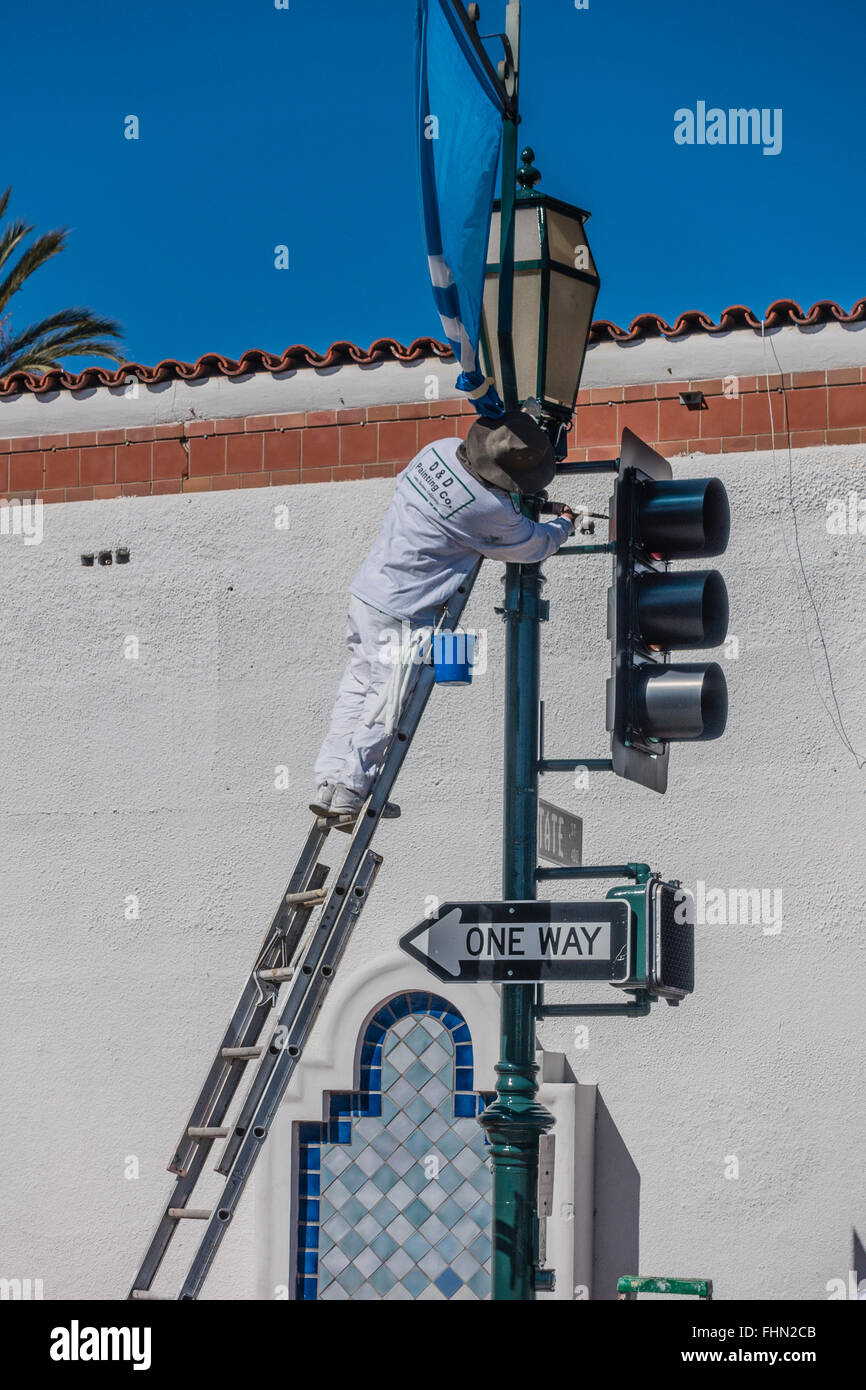 Männlichen spanischen Maler steht auf einer Leiter über seine Tropfen Tuch wie er einen Ampel-Pol malt. Stockfoto