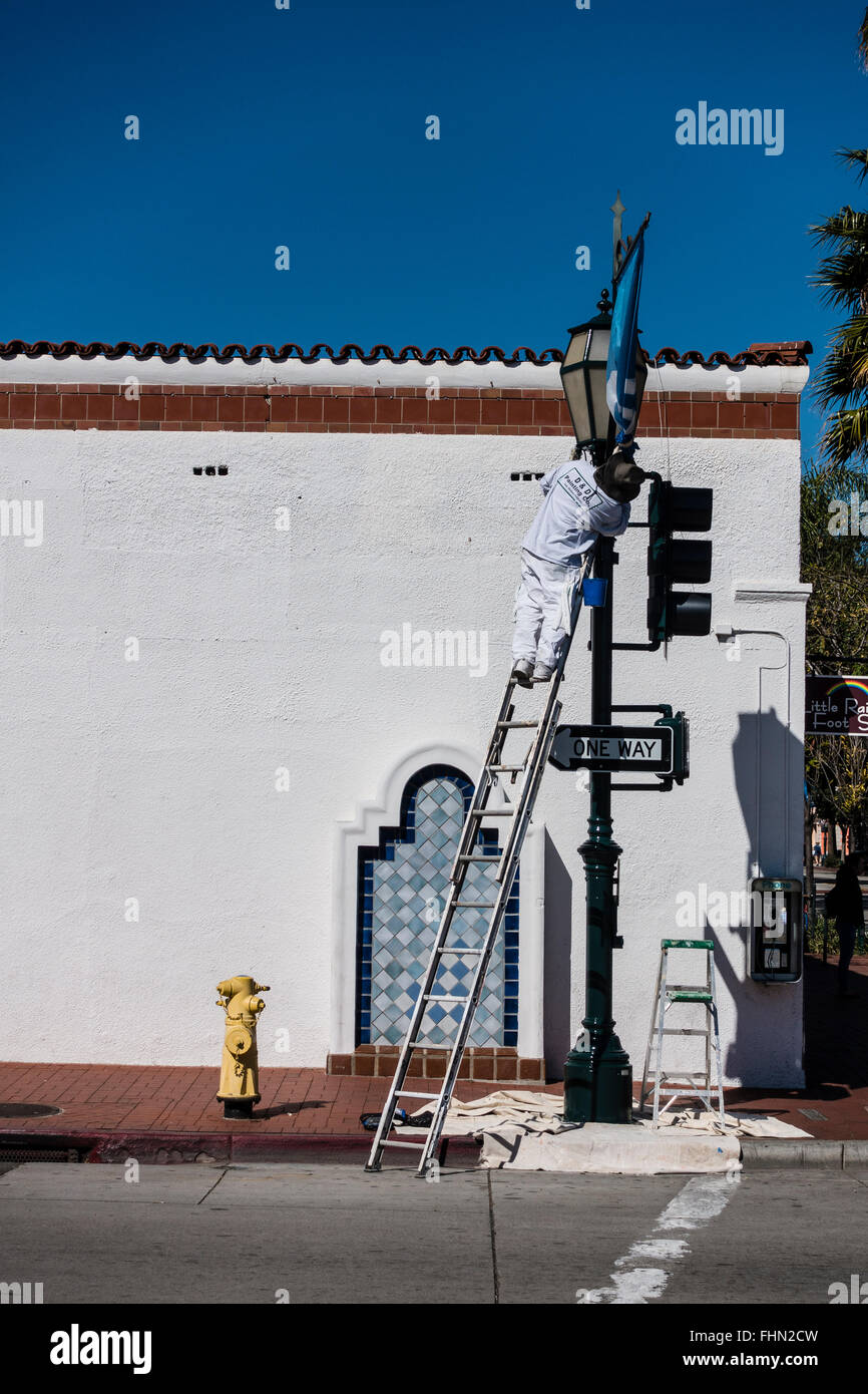 Männlichen spanischen Maler steht auf einer Leiter über seine Tropfen Tuch wie er einen Ampel-Pol malt. Stockfoto