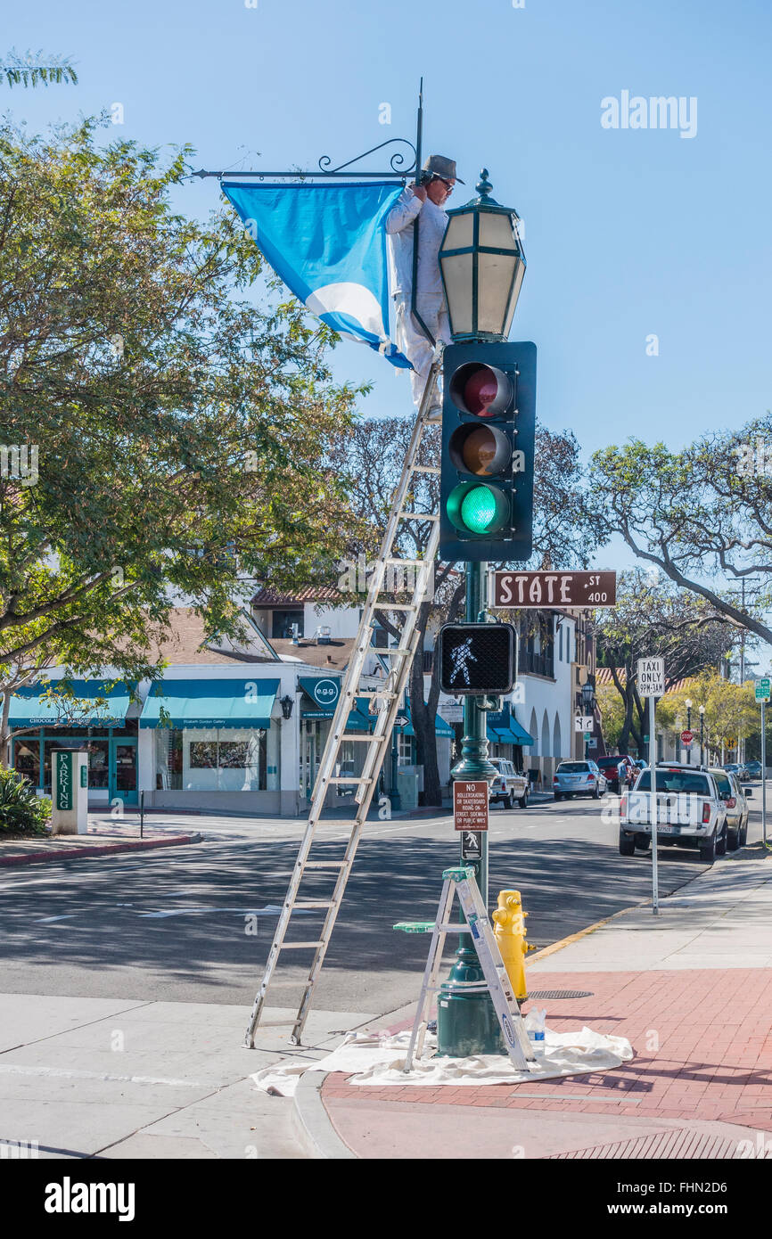 Männlichen spanischen Maler steht auf einer Leiter über seine Tropfen Tuch wie er einen Ampel-Pol malt. Stockfoto