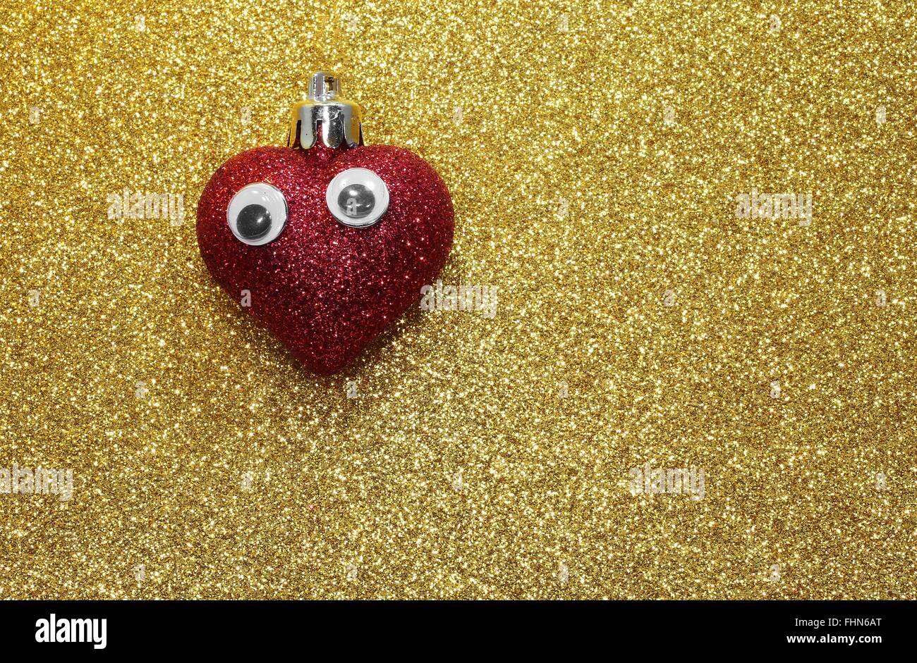 isolierte rotes Herz mit Augen auf dem goldenen Hintergrund glänzend Stockfoto