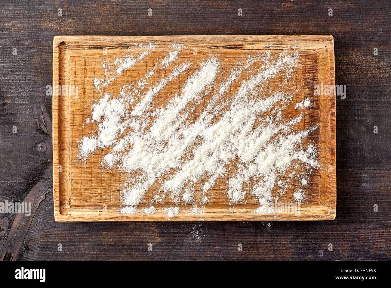 Weißes Mehl auf Holzbrett auf dunklen Holztisch, Ansicht von oben Stockfoto