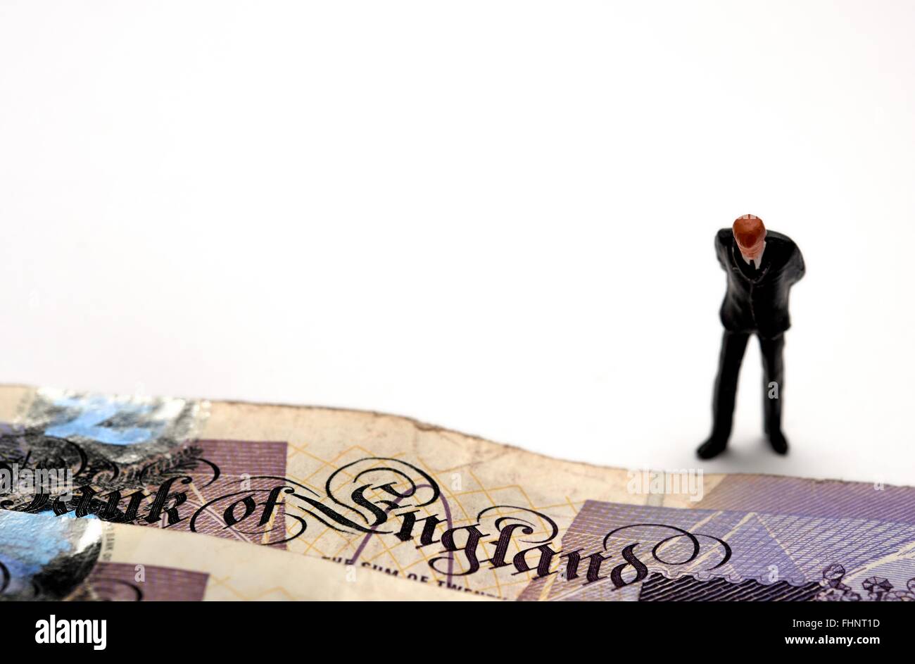 Eine Miniatur Figur Geschäftsmann im Anzug blickte auf die Worte Bank Of England auf einige zwanzig Pfund-Noten Stockfoto