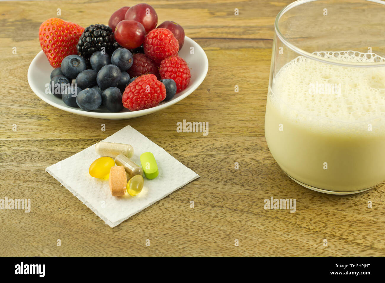 Beeren, antioxidative Nahrungsergänzungsmittel und eine Tasse Sojamilch auf Holztisch Stockfoto