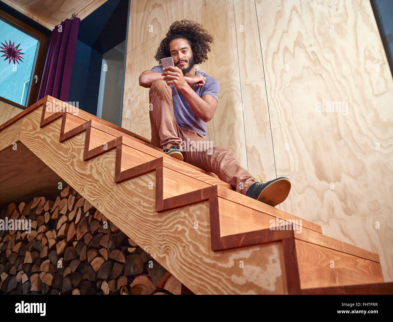 Junger Mann auf Holztreppen Blick auf Handy Stockfoto
