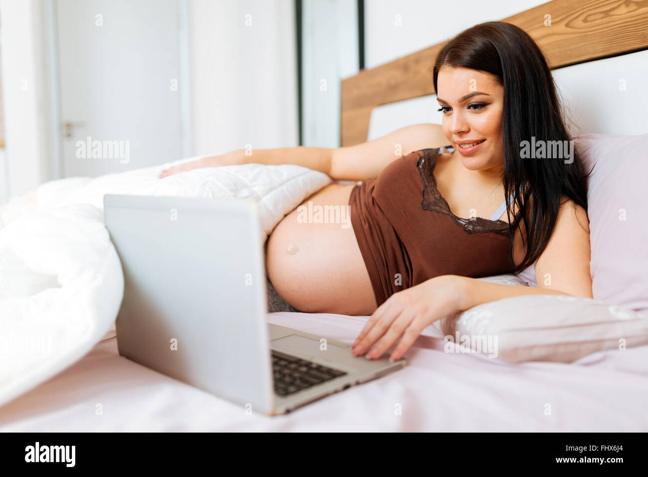 Schöne schwangere Frau mit Laptop im Bett beim Ausruhen Stockfoto