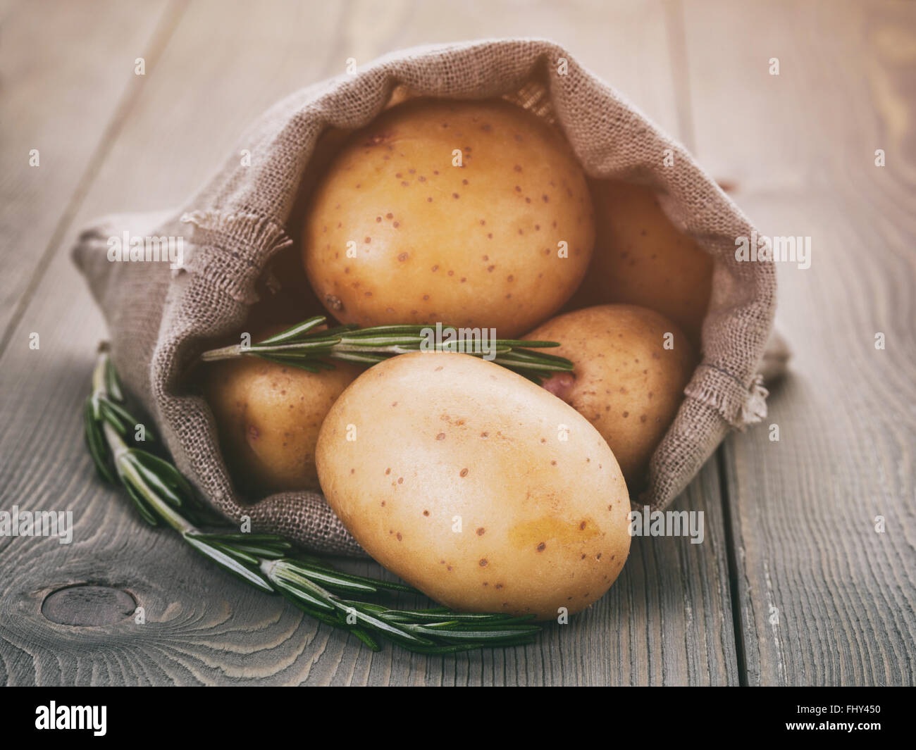 Babykartoffeln in Sack Tasche mit Rosmarin auf Holztisch Stockfoto