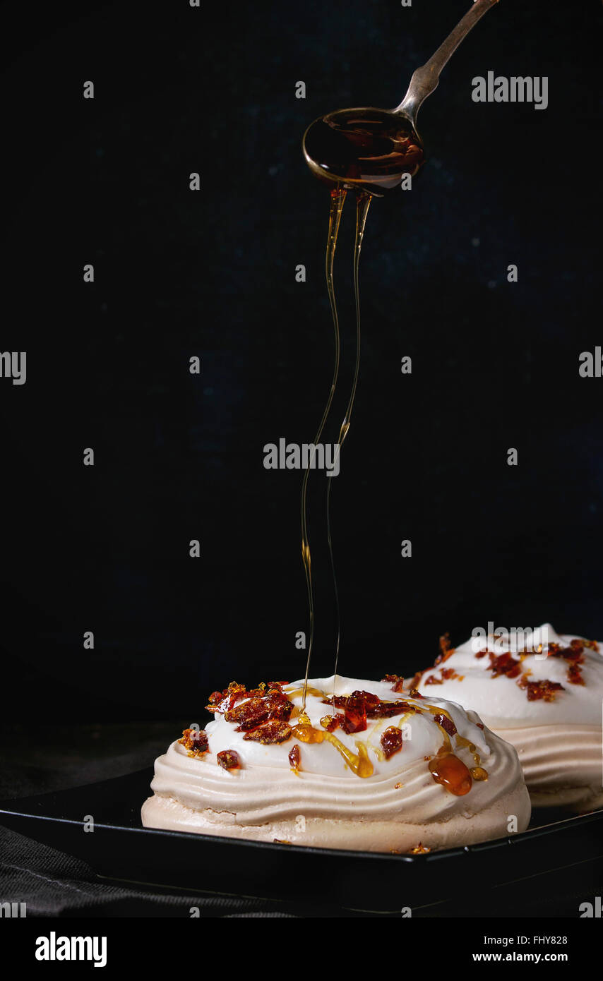 Schwarze Platte mit Baiser Dessert Pavlova mit Karamell Einschalten von Karamell-Sauce. Auf grau Textil Serviette über dunklen Tisch. Stockfoto