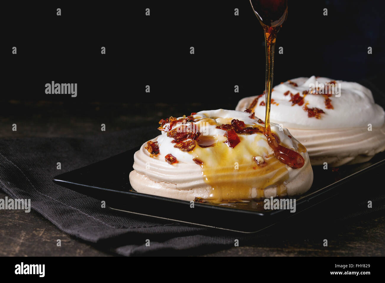 Schwarze Platte mit Baiser Dessert Pavlova mit Karamell Einschalten von Karamell-Sauce. Auf grau Textil Serviette über dunklen Tisch. Stockfoto