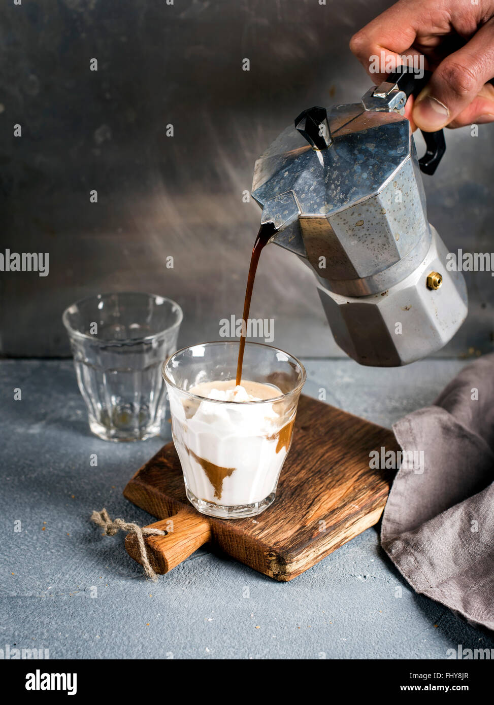 Ein Glas Kaffee mit Eis auf einem rustikalen Holzbrett. Getränk wird aus einer italienischen Moka-Stahltopf Besitz des Mannes Hand Gre gegossen. Stockfoto