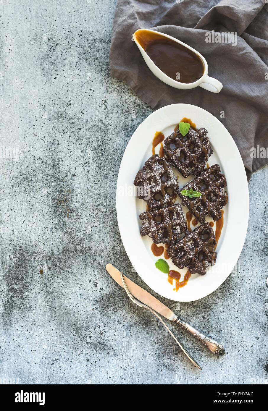 Schokolade, belgische Waffeln mit gesalzenem Karamell-Sauce und Minze auf weißer Keramik Teller über Grunge Hintergrund Draufsicht co Stockfoto