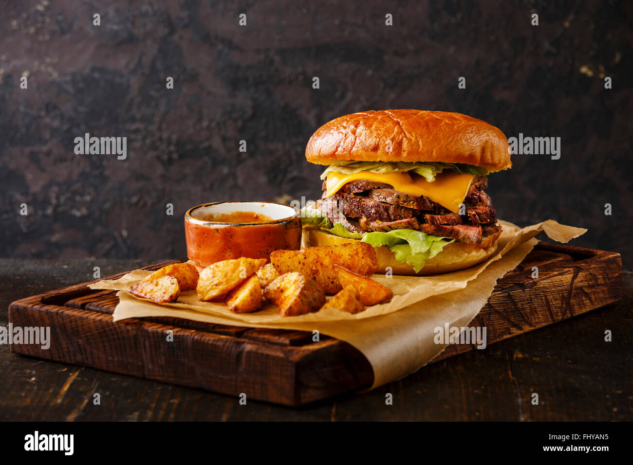 Pastrami-Burger-Imbiss-Snack mit in Scheiben geschnittenen Braten Rindfleisch und Kartoffel Wedges auf dunklem Hintergrund Stockfoto