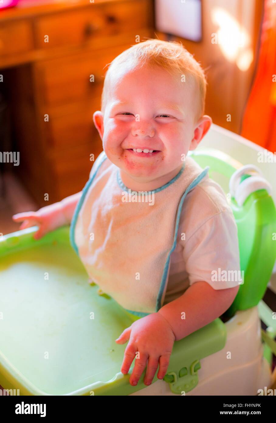 -MODELL VERÖFFENTLICHT. Kleinkind in einen Hochstuhl, lächelnd in Richtung Kamera. Stockfoto