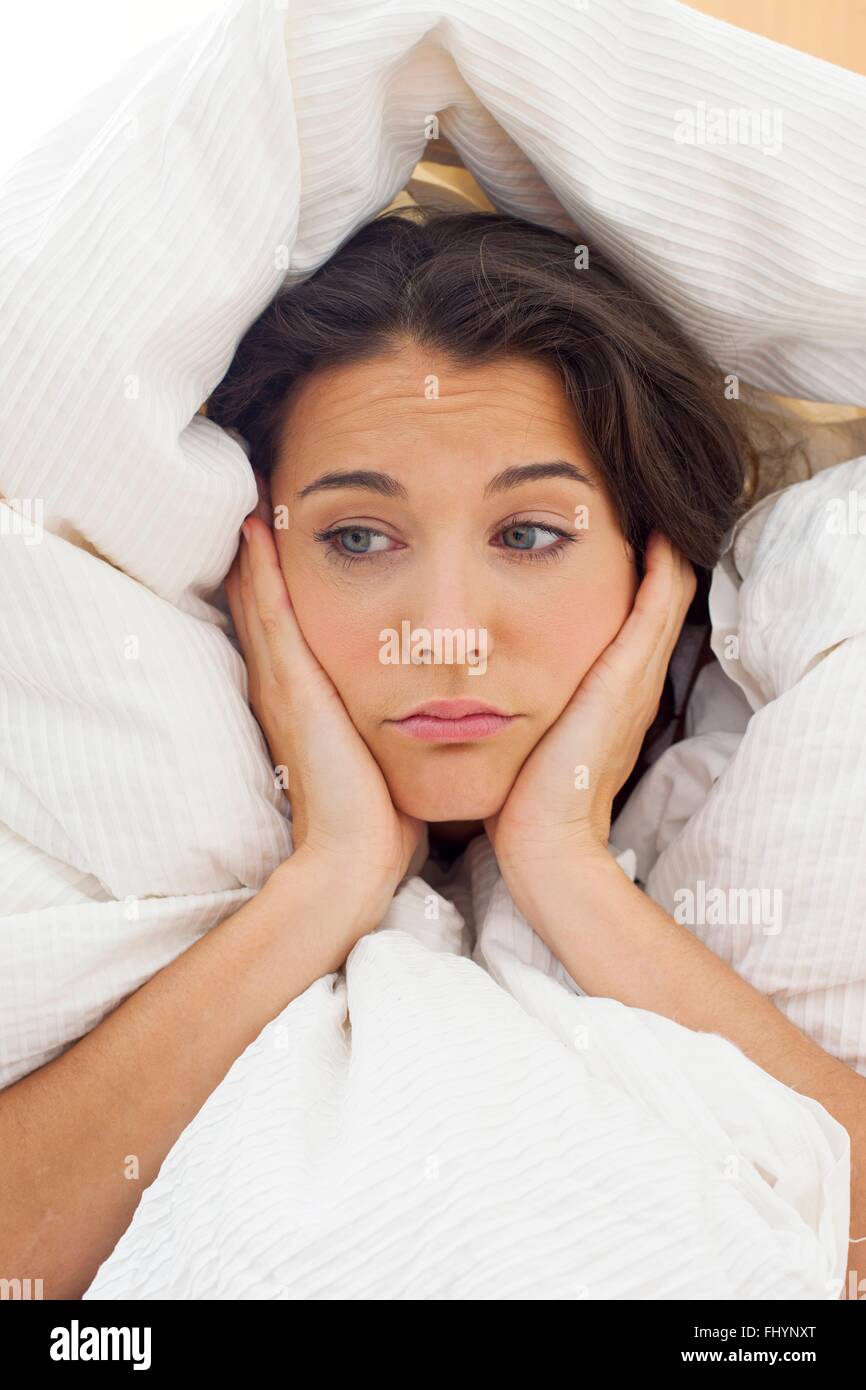 -MODELL VERÖFFENTLICHT. Frau im Bett unter die Bettwäsche mit den Händen an ihr Kinn. Stockfoto