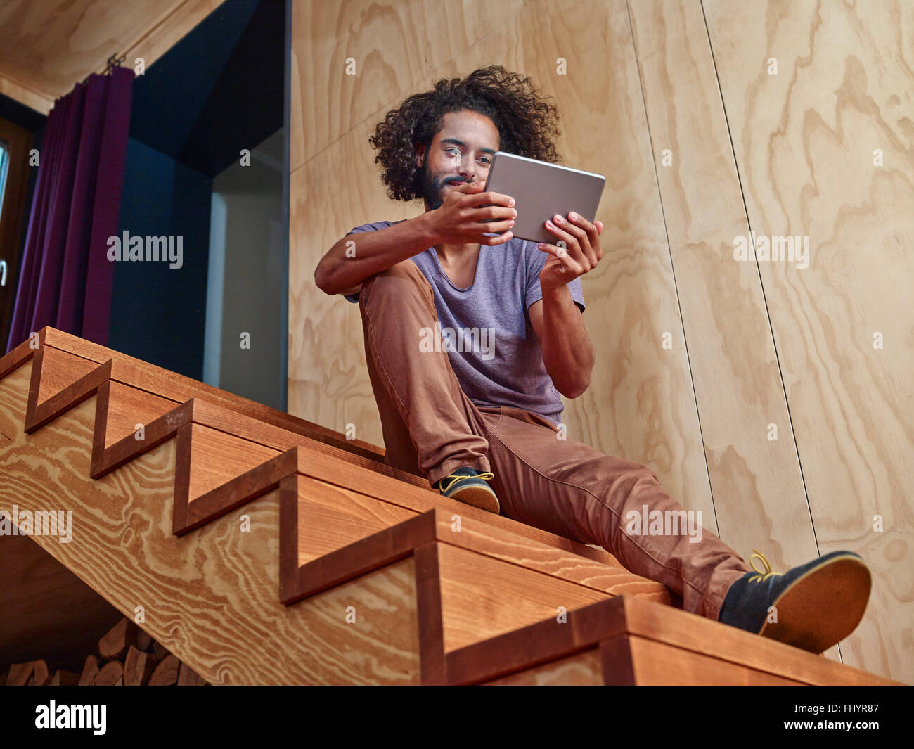 Junger Mann auf Holztreppen Blick auf digital-Tablette Stockfoto