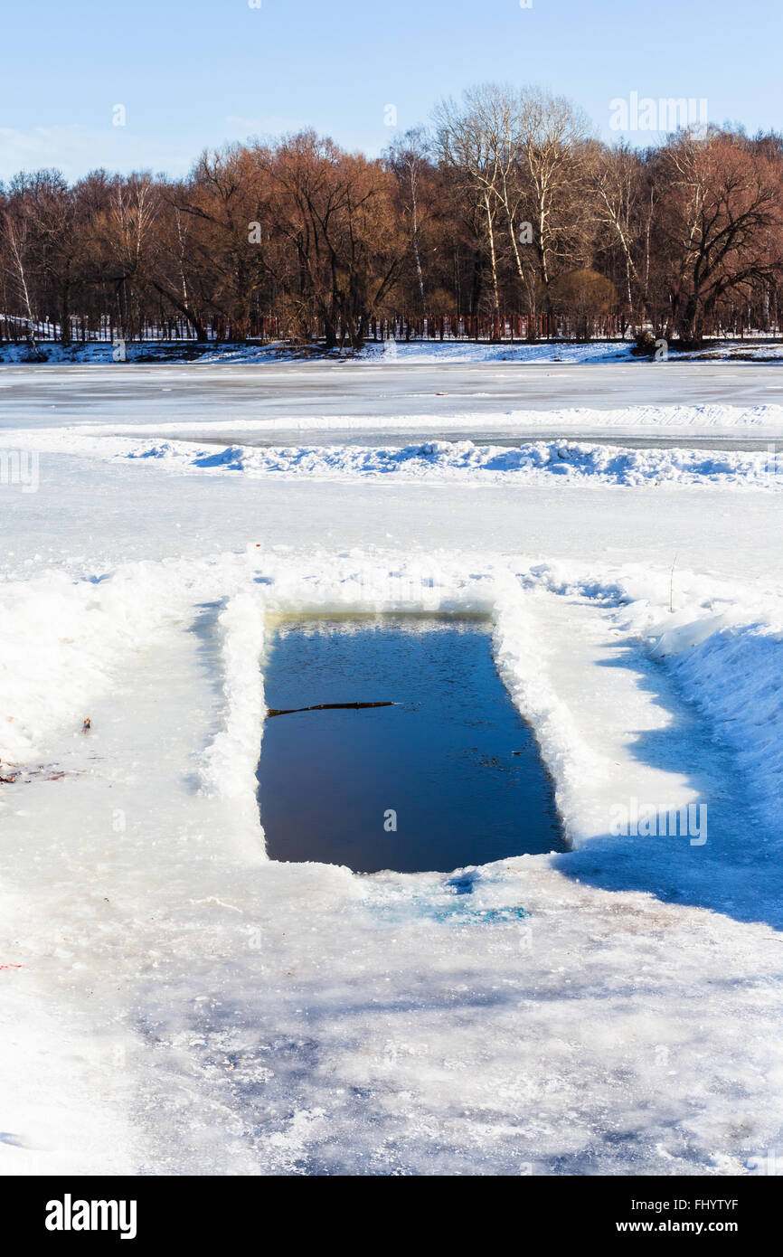 Eisloch im zugefrorenen Teich im sonnigen Wintertag Stockfoto